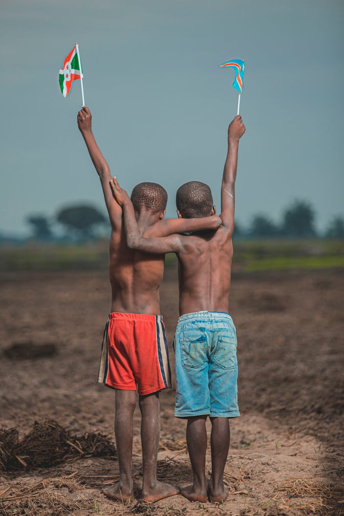 Two boys holding flags of Burundi and Congo, standing in a field, celebrating friendship.