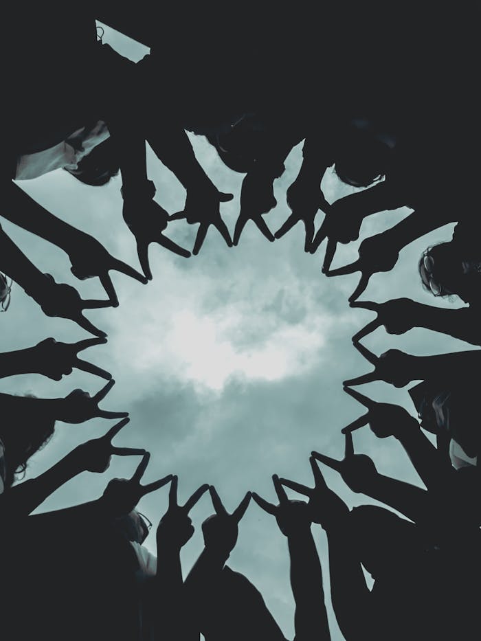 Silhouette of people forming a star with hands against a cloudy sky.